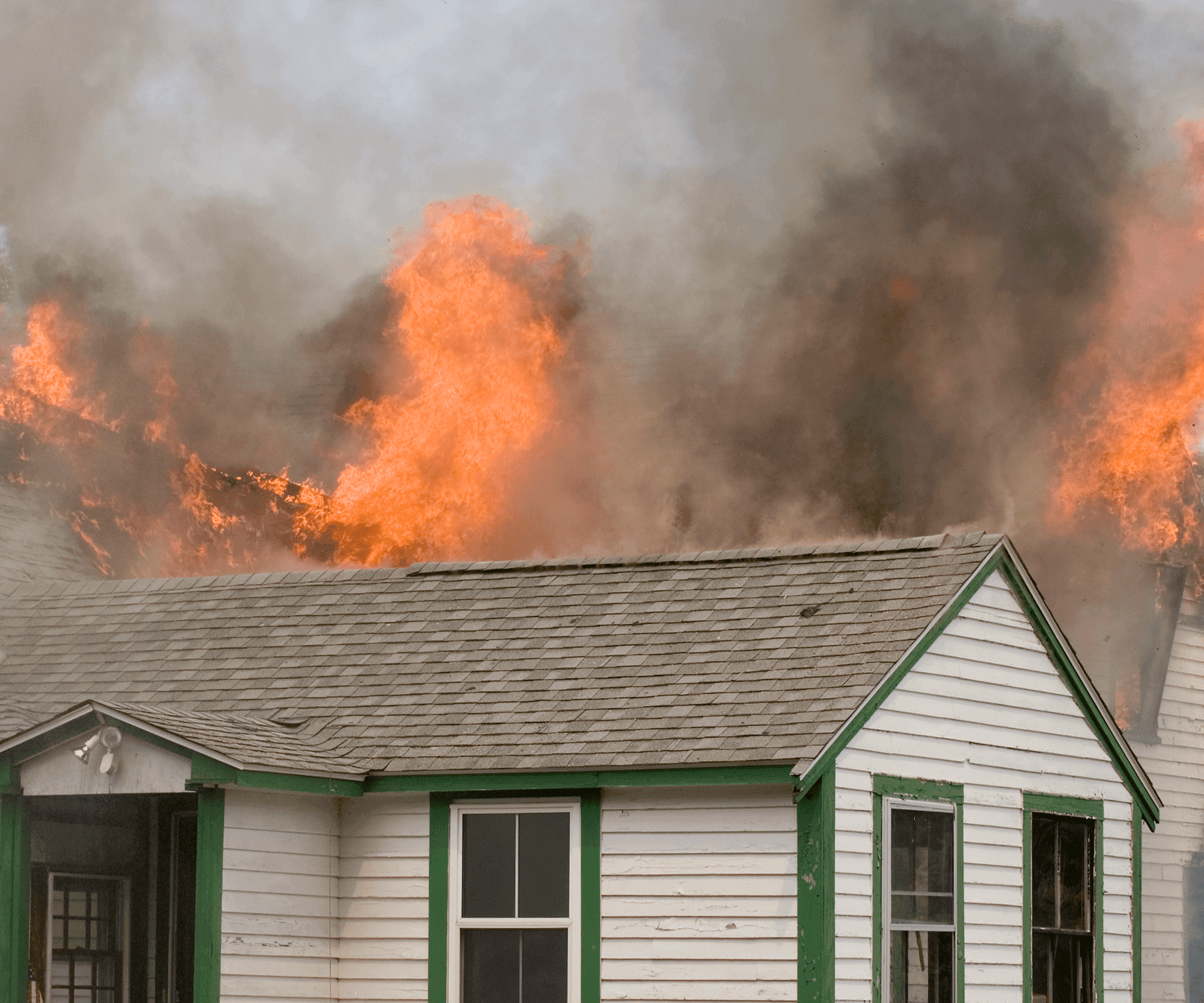Flames and smoke engulf a house roof during a fire.