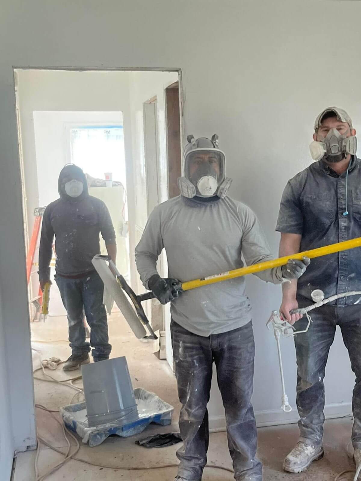 Three workers wearing masks and holding tools in a construction area.